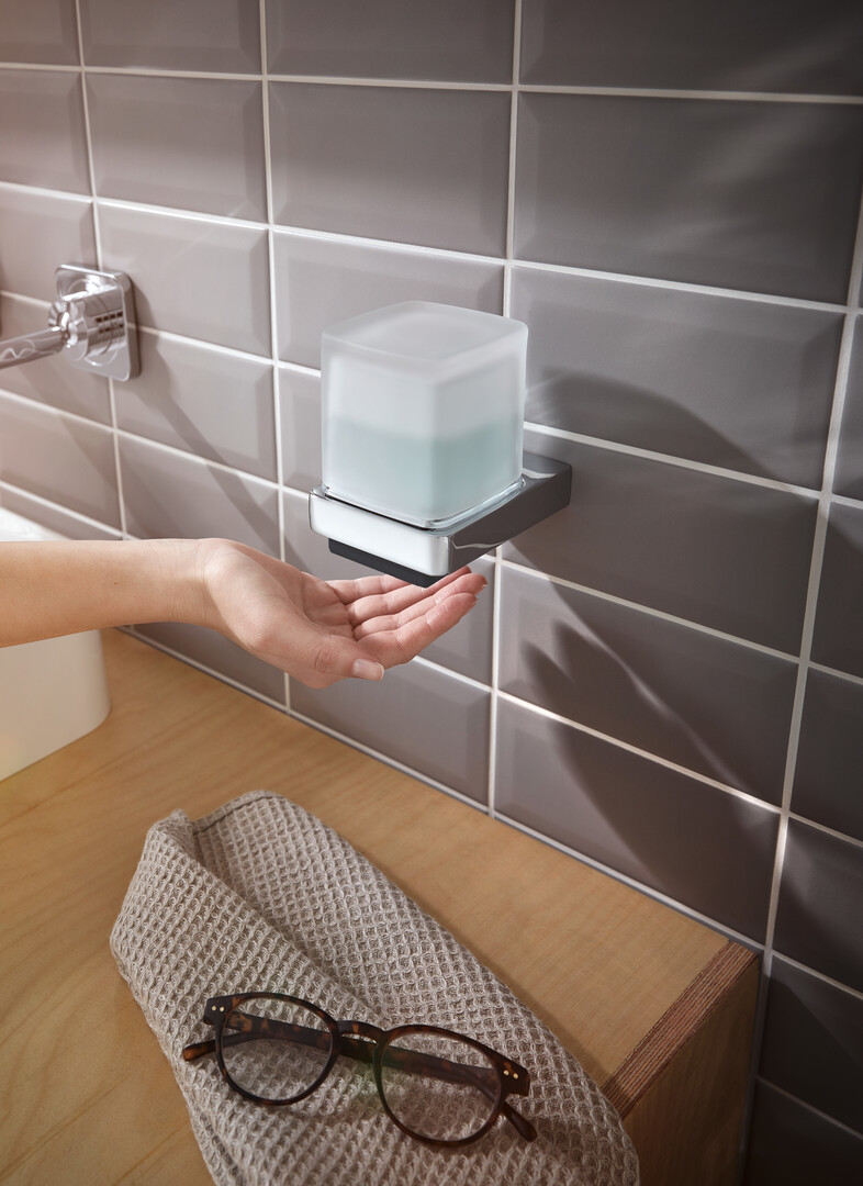 Hand unter modernem Wand-Seifenspender mit grauen Fliesen