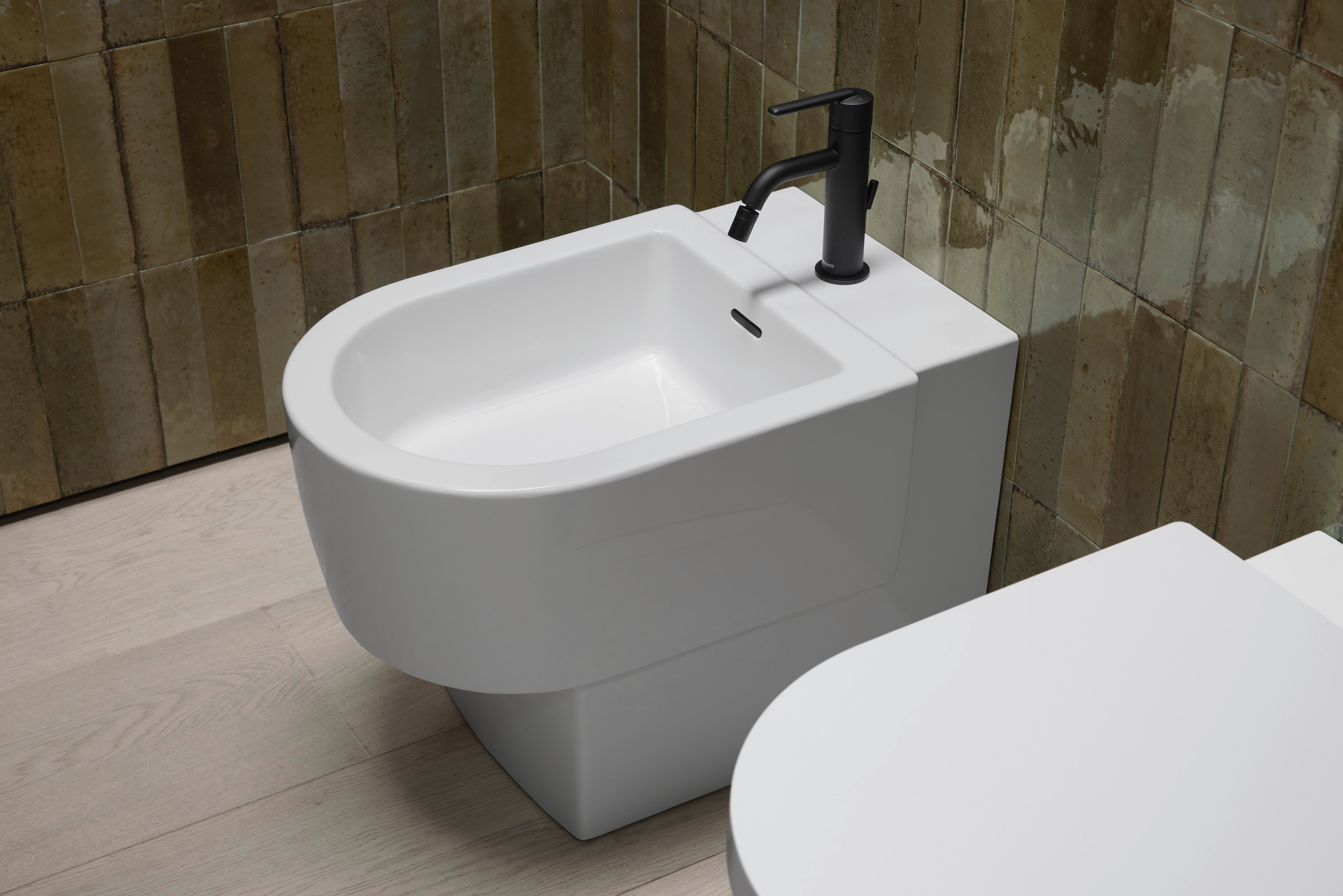 Weißes Bidet mit schwarzem Wasserhahn vor braunen Wandfliese
