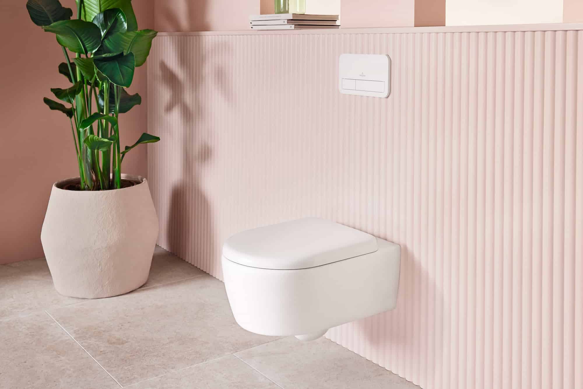 Wandhängende weiße Toilette neben großer Topfpflanze vor ros